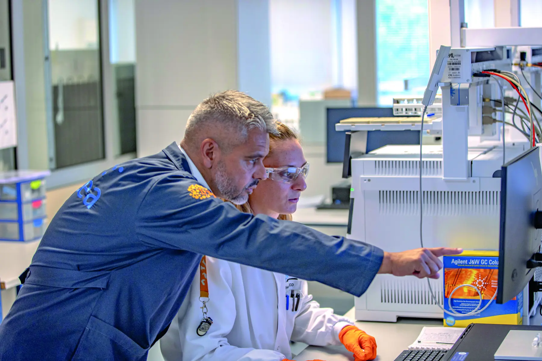 Un chercheur de l’IRSEA explique une analyse à une collègue devant un appareil de laboratoire